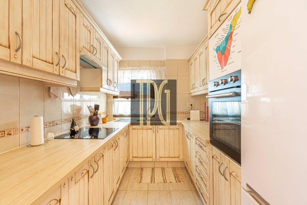 L-shaped kitchen with light wood cabinets, beige countertops, and built-in oven on the right wall.