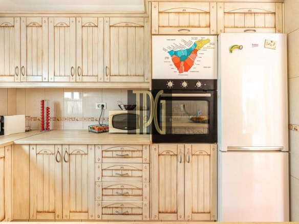 Kitchen with light wood cabinets, built-in oven, microwave, and a tall white refrigerator; map poster on the oven door
