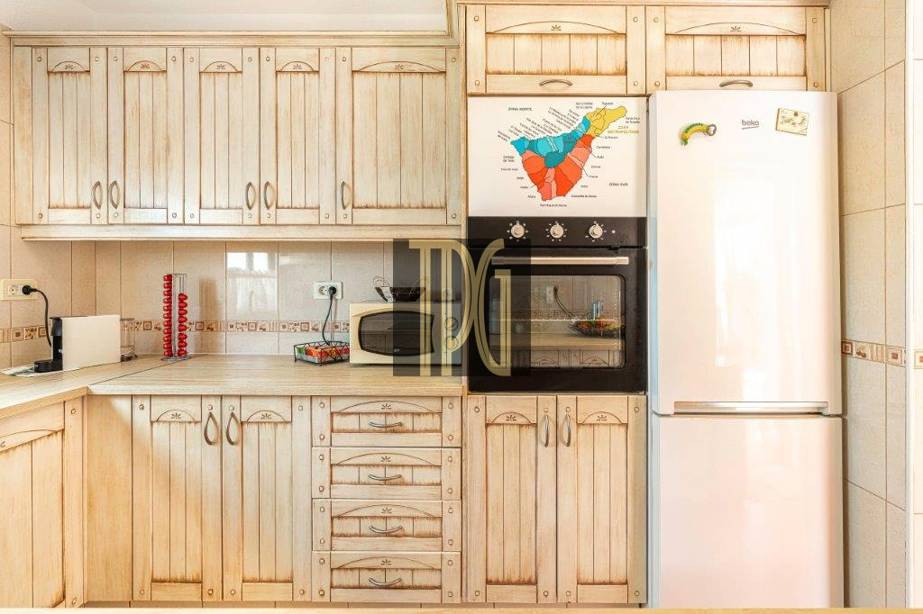 Kitchen with light wood cabinets, built-in oven, microwave, and a tall white refrigerator; map poster on the oven door