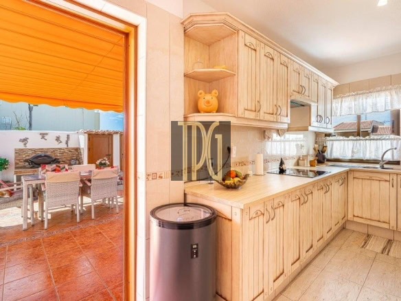 Bright kitchen with light wood cabinets and beige countertops, opening to an outdoor dining area under an orange awning.