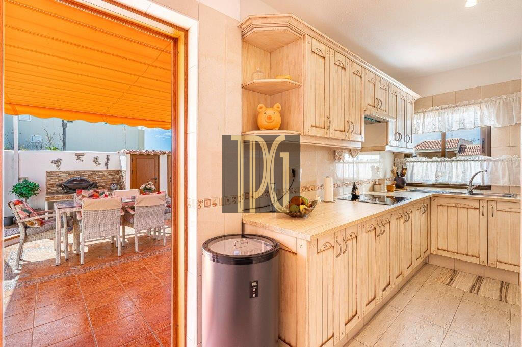 Bright kitchen with light wood cabinets and beige countertops, opening to an outdoor dining area under an orange awning.