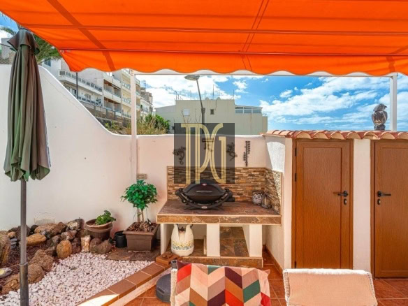 Backyard patio under an orange canopy with a built-in grill, tile counter, and two wooden storage doors.