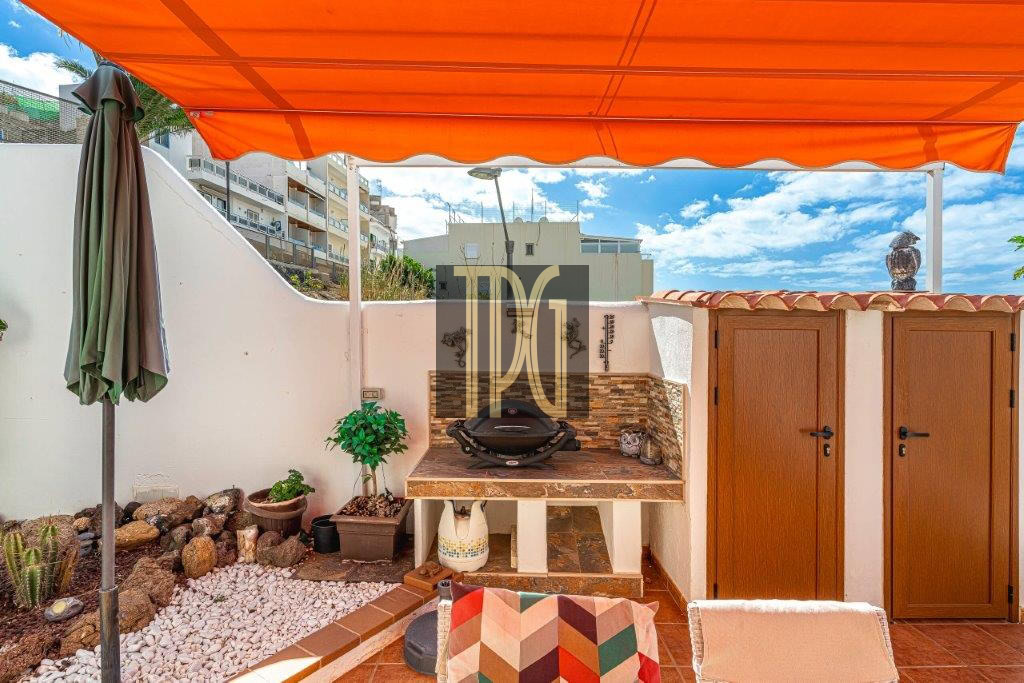 Backyard patio under an orange canopy with a built-in grill, tile counter, and two wooden storage doors.