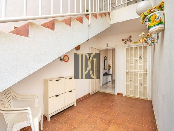 Covered patio with terracotta tiles, white walls, a plastic chair, a cabinet, and glass doors opening to an interior room, under a stairwell.