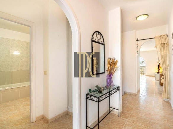 Bright hallway with an arched doorway to a tiled bathroom on the left, and a black metal console table with a mirror on the wall.