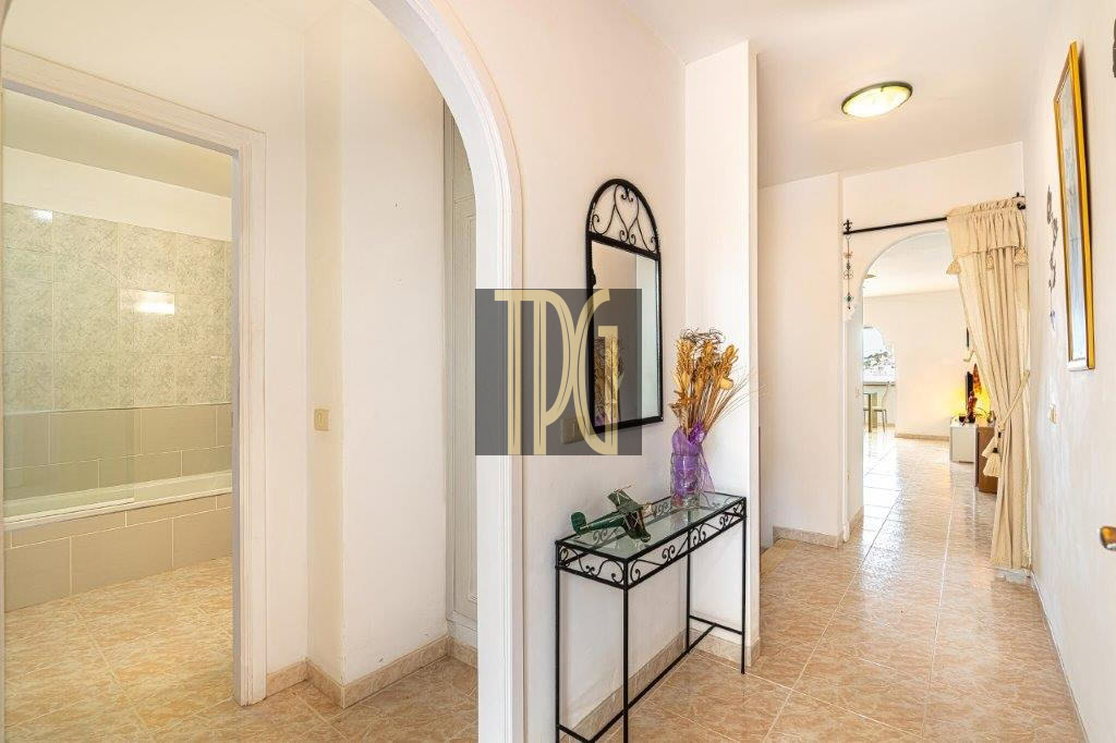 Bright hallway with an arched doorway to a tiled bathroom on the left, and a black metal console table with a mirror on the wall.