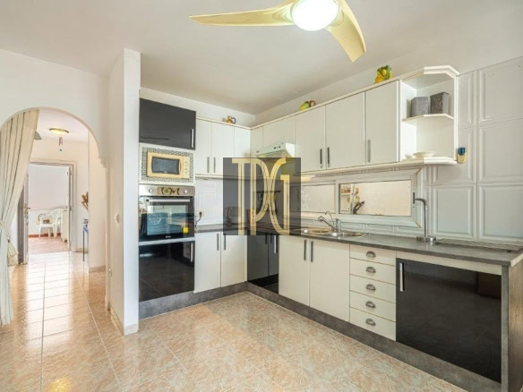 Modern kitchen with white cabinets, stainless appliances, and a curved arched doorway leading to a sunlit dining area; tile floor and wide counter space visible.