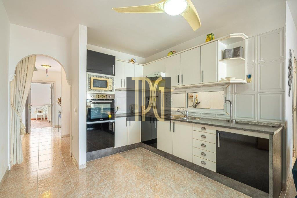Modern kitchen with white cabinets, stainless appliances, and a curved arched doorway leading to a sunlit dining area; tile floor and wide counter space visible.