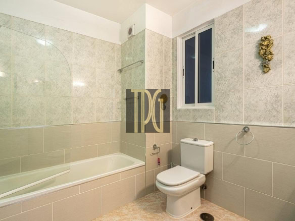 Bathroom with a white bathtub and glass shower panel, a toilet, and beige tiled walls with a small window above the toilet.