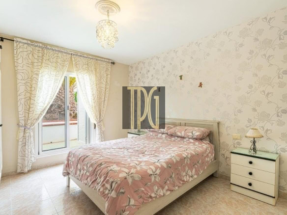 Bright bedroom with pink floral bedding, matching wallpaper, and a chandelier above the bed.