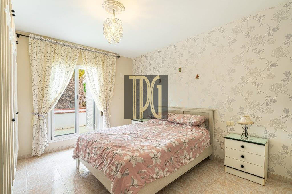 Bright bedroom with pink floral bedding, matching wallpaper, and a chandelier above the bed.