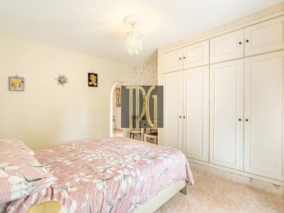 Bright bedroom with a long row of white built-in wardrobes, a pink floral duvet, and a hanging chandelier.