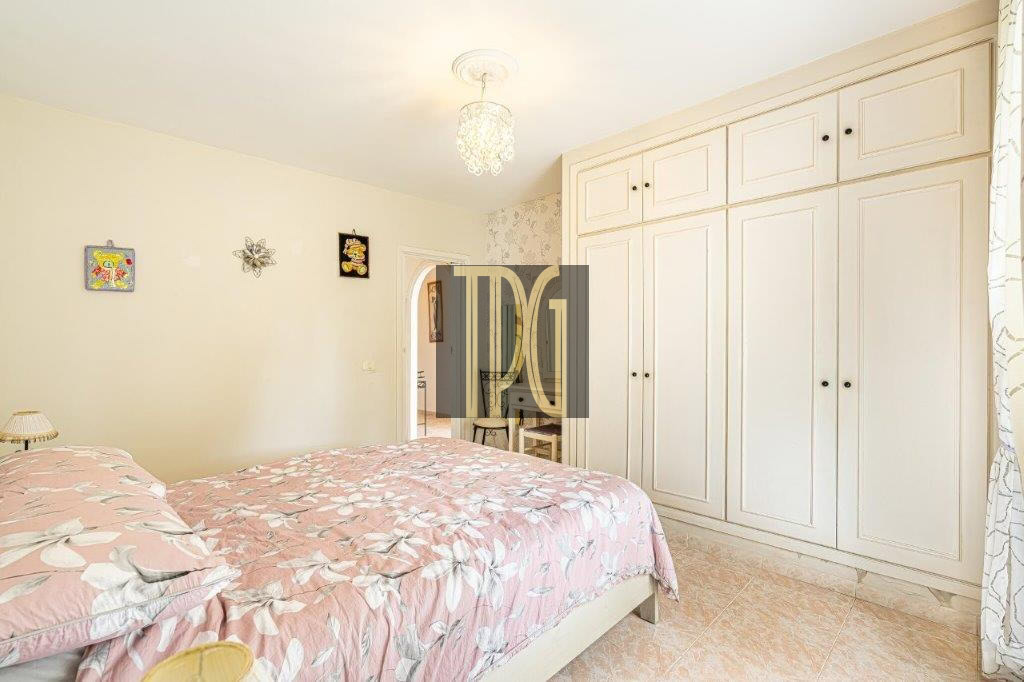 Bright bedroom with a long row of white built-in wardrobes, a pink floral duvet, and a hanging chandelier.