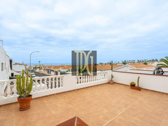 Terrace with terracotta tiles and white railing, potted cactus plants, overlooking rooftops and the sea.