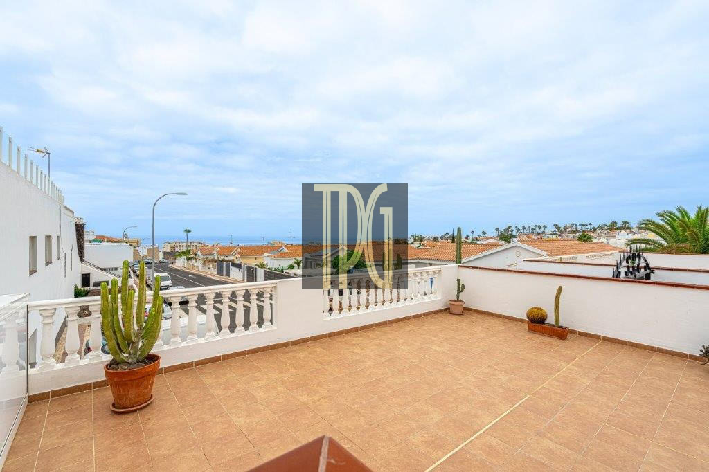 Terrace with terracotta tiles and white railing, potted cactus plants, overlooking rooftops and the sea.