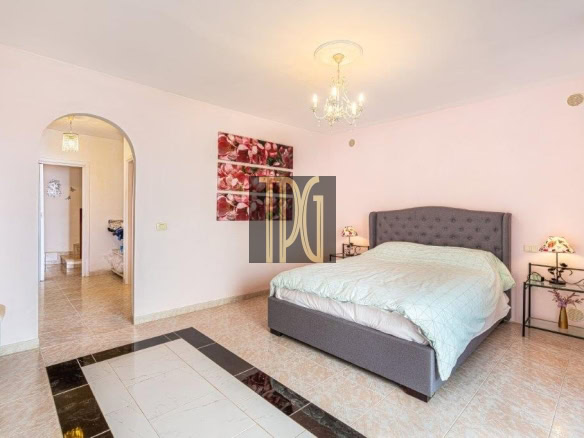 Spacious bedroom with a gray upholstered king bed, twin nightstands, chandelier, pink walls, and pink curtains.