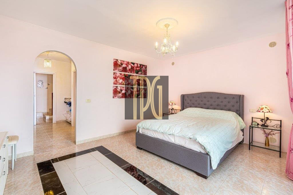 Spacious bedroom with a gray upholstered king bed, twin nightstands, chandelier, pink walls, and pink curtains.