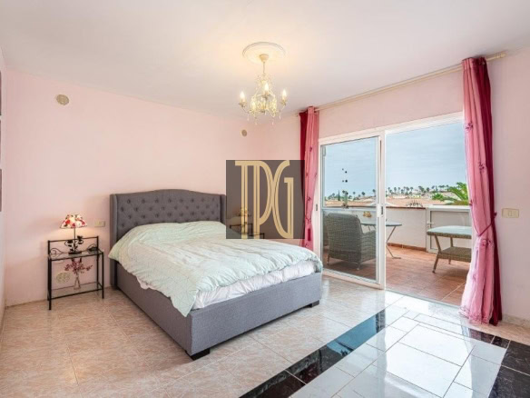Bedroom with pink walls, tufted gray bed, mint quilt, and balcony doors to a seating area with an ocean view in the distance.