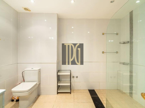 Modern white-tiled bathroom featuring a toilet, a small gray shelving cart, and a glass-enclosed shower on the right; beige tiled floor and wall-mounted towel racks create a clean, minimalist look.