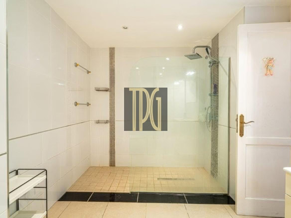 White-tiled bathroom with a glass-walled walk-in shower and rainfall showerhead, bright and modern.