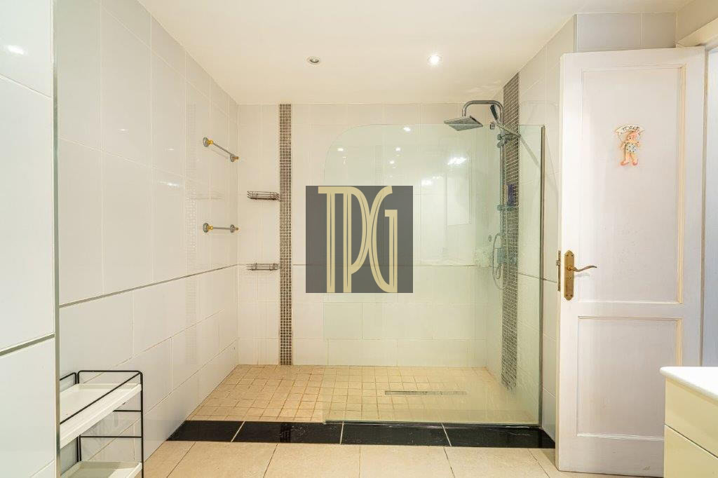 White-tiled bathroom with a glass-walled walk-in shower and rainfall showerhead, bright and modern.
