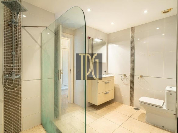 Modern bright bathroom with glass shower partition, beige floating vanity, and toilet.