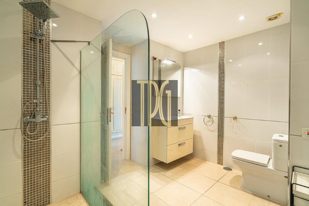 Modern bright bathroom with glass shower partition, beige floating vanity, and toilet.