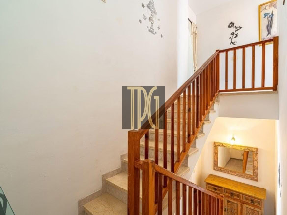 Wooden staircase with a railing leading to a bright upper landing, seen from the lower stairs.