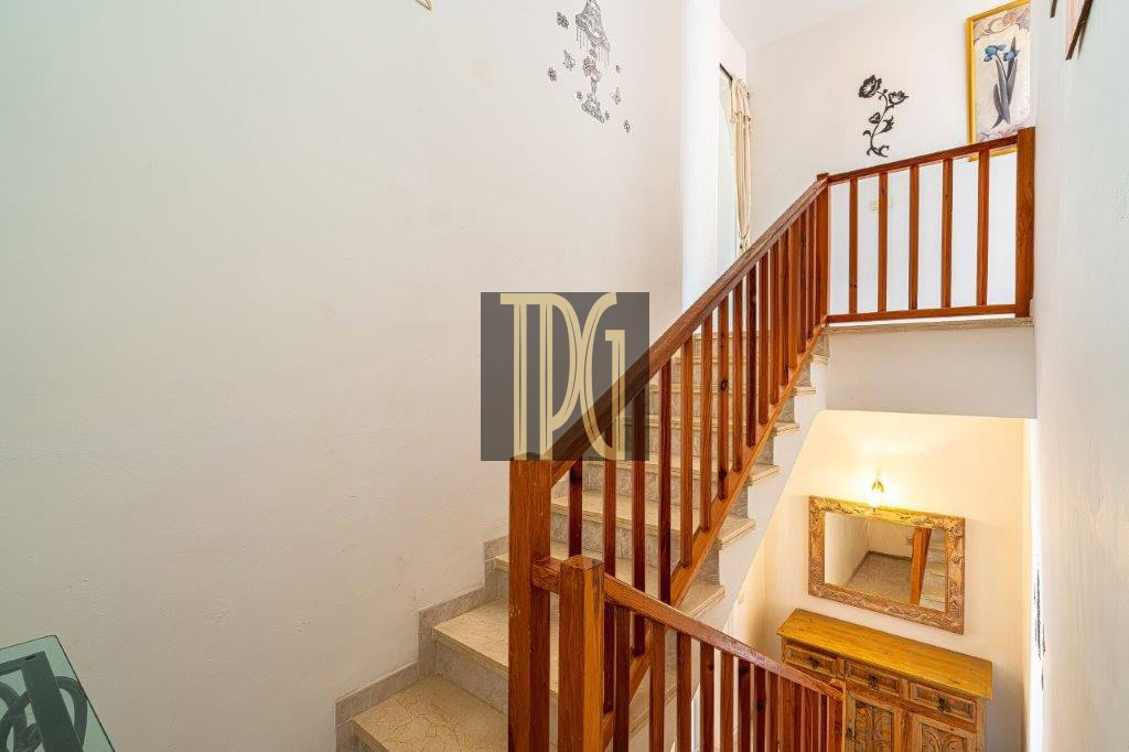 Wooden staircase with a railing leading to a bright upper landing, seen from the lower stairs.