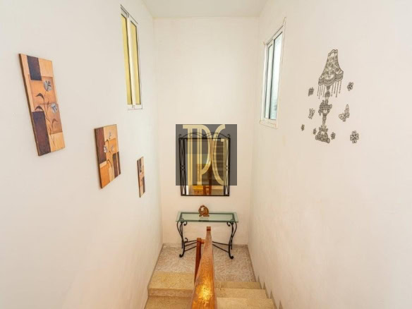 Narrow stairwell with white walls, wooden handrail, and small framed art on the left; a glass-topped console table and mirror at the bottom, plus wall decals on the right.