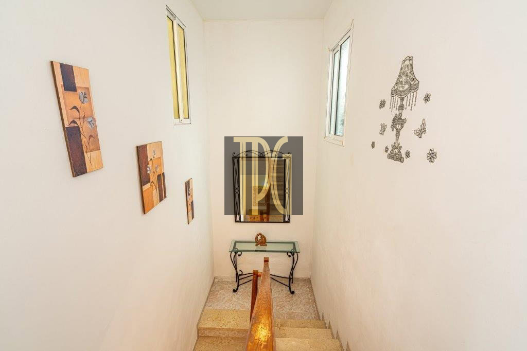 Narrow stairwell with white walls, wooden handrail, and small framed art on the left; a glass-topped console table and mirror at the bottom, plus wall decals on the right.
