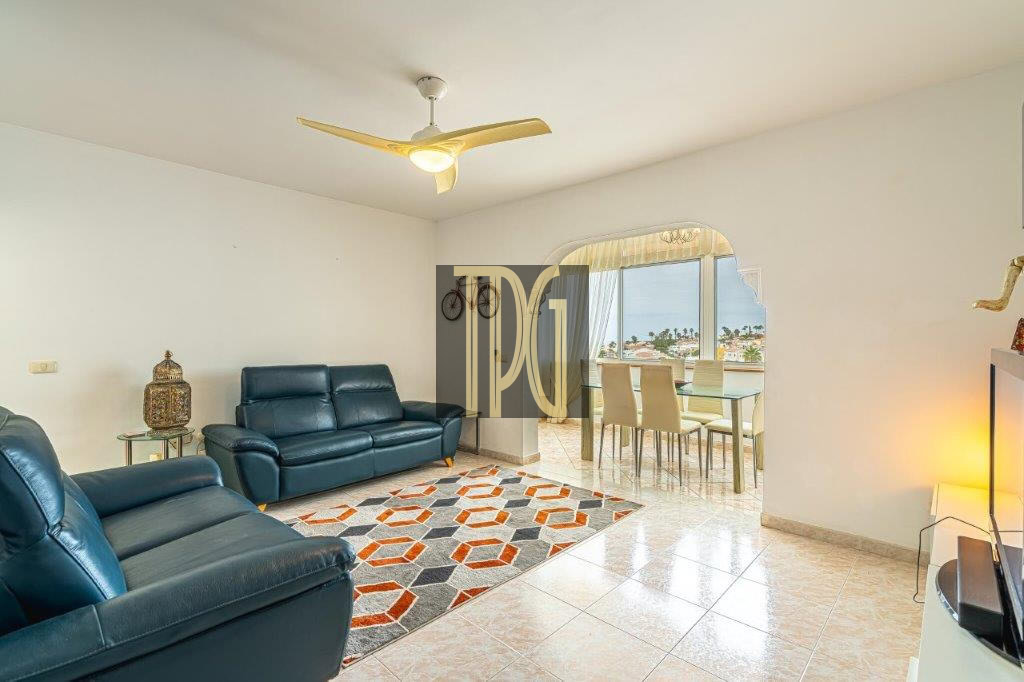 Living room with blue leather sofa set, geometric rug, and a dining area by a balcony with an ocean view.