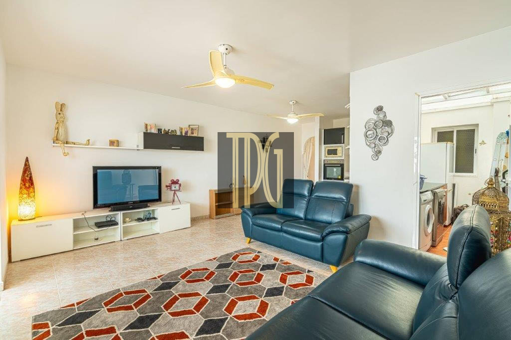 Bright living room with blue leather sofas, a geometric red-gray rug, and a wall-mounted TV on white entertainment unit.
