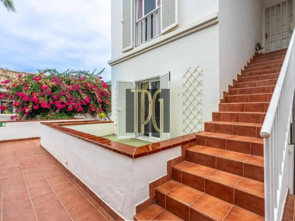 Terracotta tiled patio with a white building, pink bougainvillea, and a wide staircase with a white railing leading up the side.
