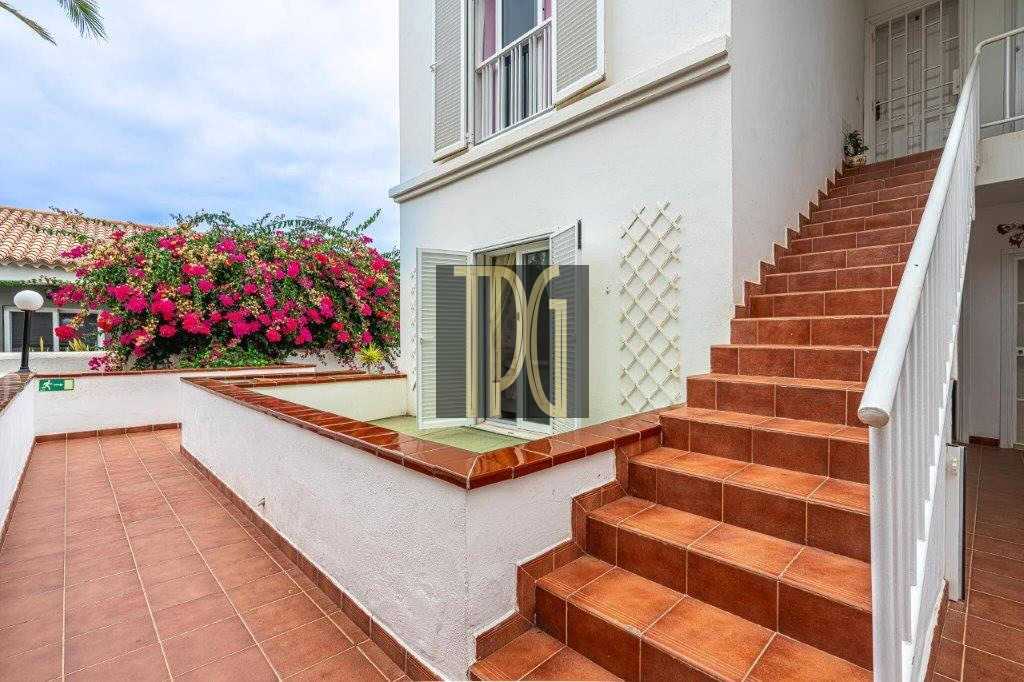 Terracotta tiled patio with a white building, pink bougainvillea, and a wide staircase with a white railing leading up the side.
