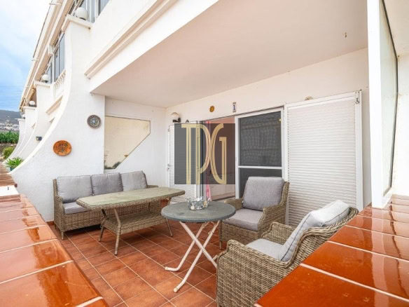 Outdoor balcony seating area with wicker sofa and chairs around a round metal table on terracotta tiles.