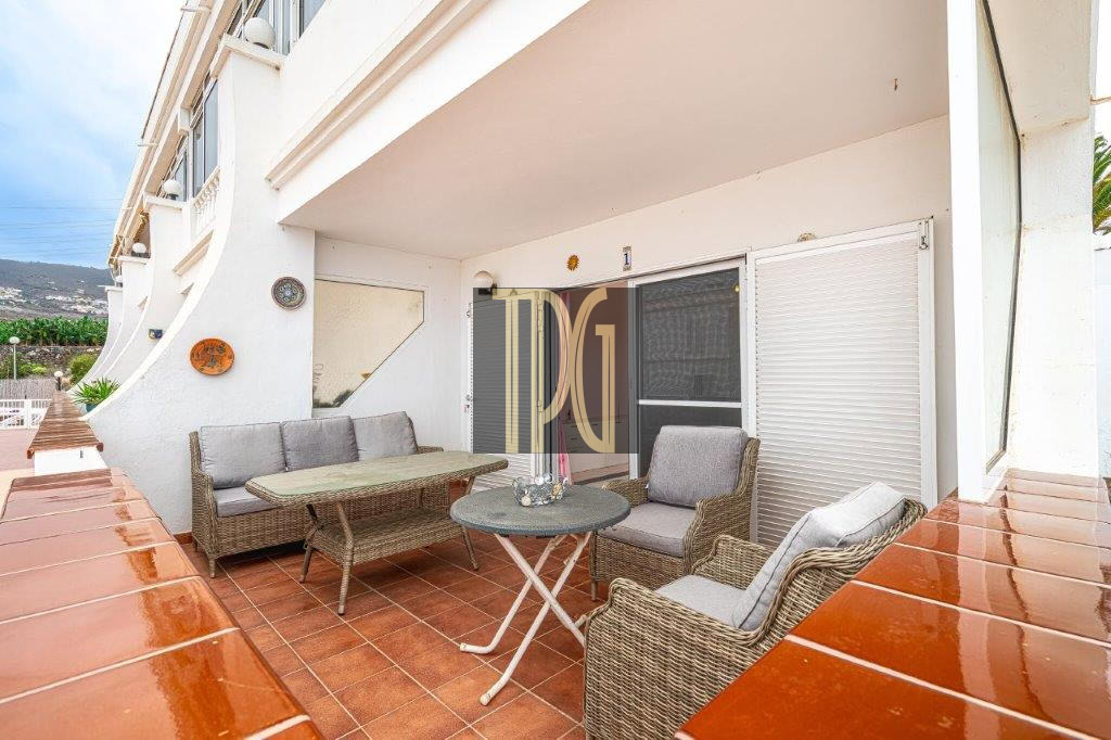 Outdoor balcony seating area with wicker sofa and chairs around a round metal table on terracotta tiles.