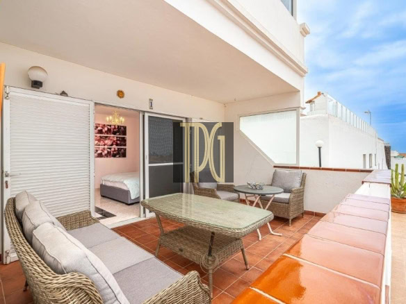 Terrace with wicker sofa set and glass table, overlooking a sunny white balcony with a potted cactus nearby and a bedroom visible through sliding doors