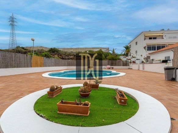 Backyard with a round swimming pool and a circular grassy island with planters on a terracotta patio under a blue sky.