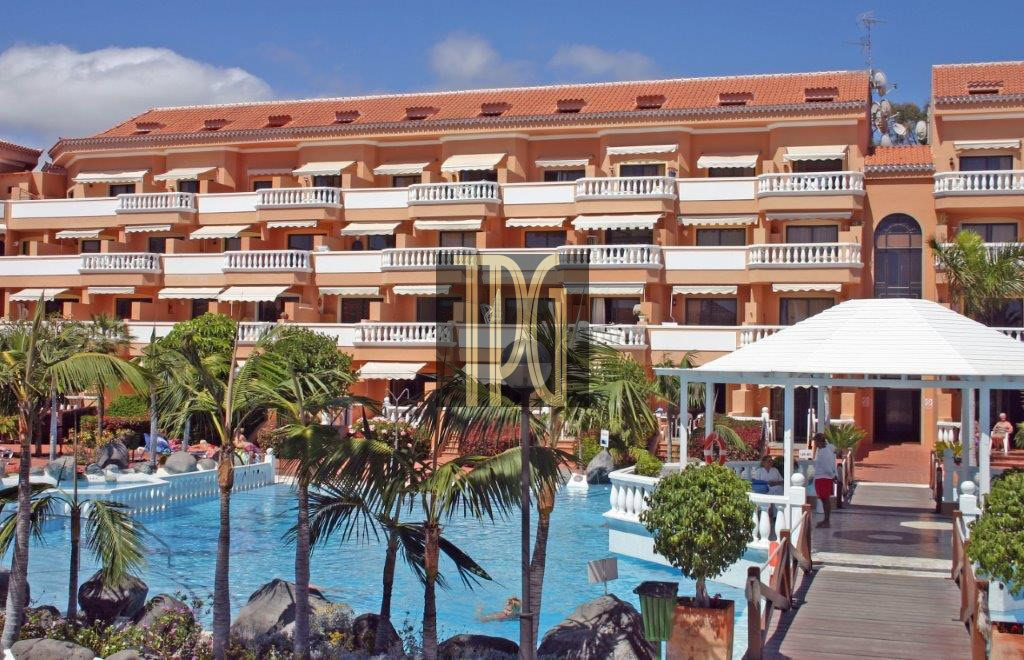 Resort hotel with orange exterior, white balconies, and a blue swimming pool surrounded by palm trees.