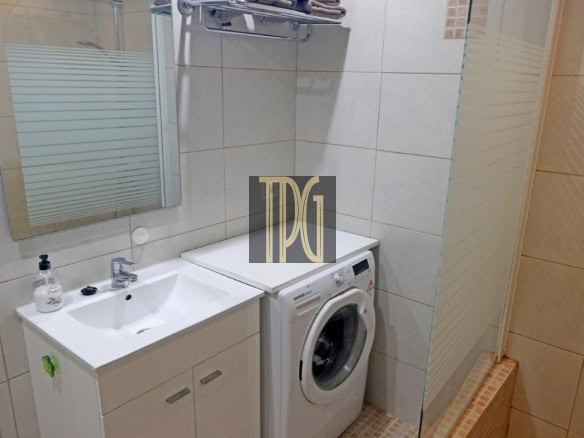 Small bathroom with a white sink, vanity, mirror, and a front-loading washing machine beside a glass shower enclosure.