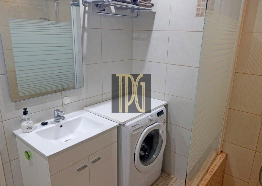 Small bathroom with a white sink, vanity, mirror, and a front-loading washing machine beside a glass shower enclosure.