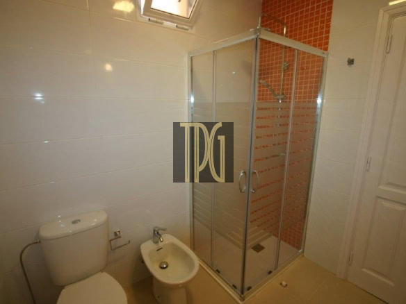 Small bathroom with a toilet, bidet, and glass shower enclosure against an orange-tiled wall.
