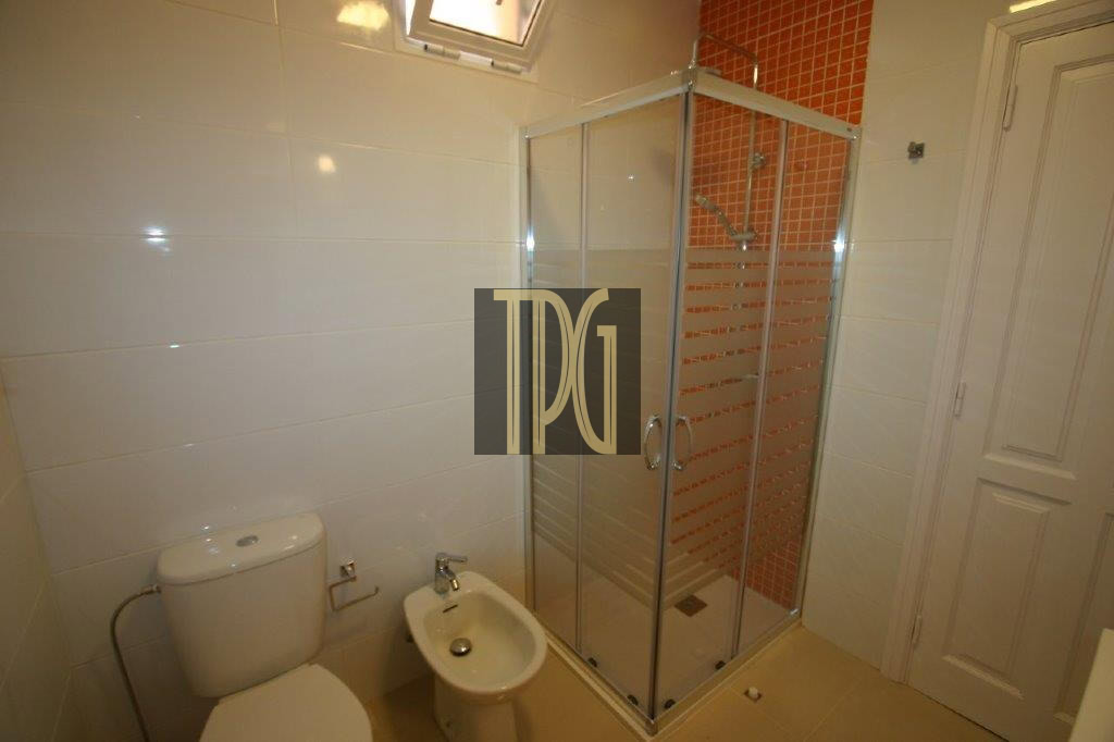 Small bathroom with a toilet, bidet, and glass shower enclosure against an orange-tiled wall.