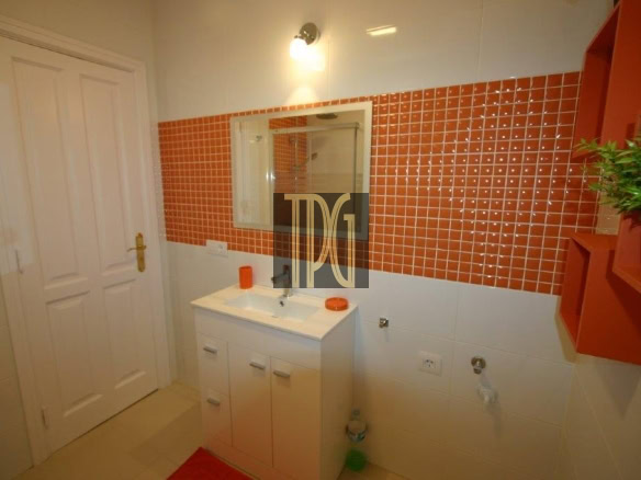 White bathroom vanity with sink in front of an orange mosaic-tile wall and a mirror above it