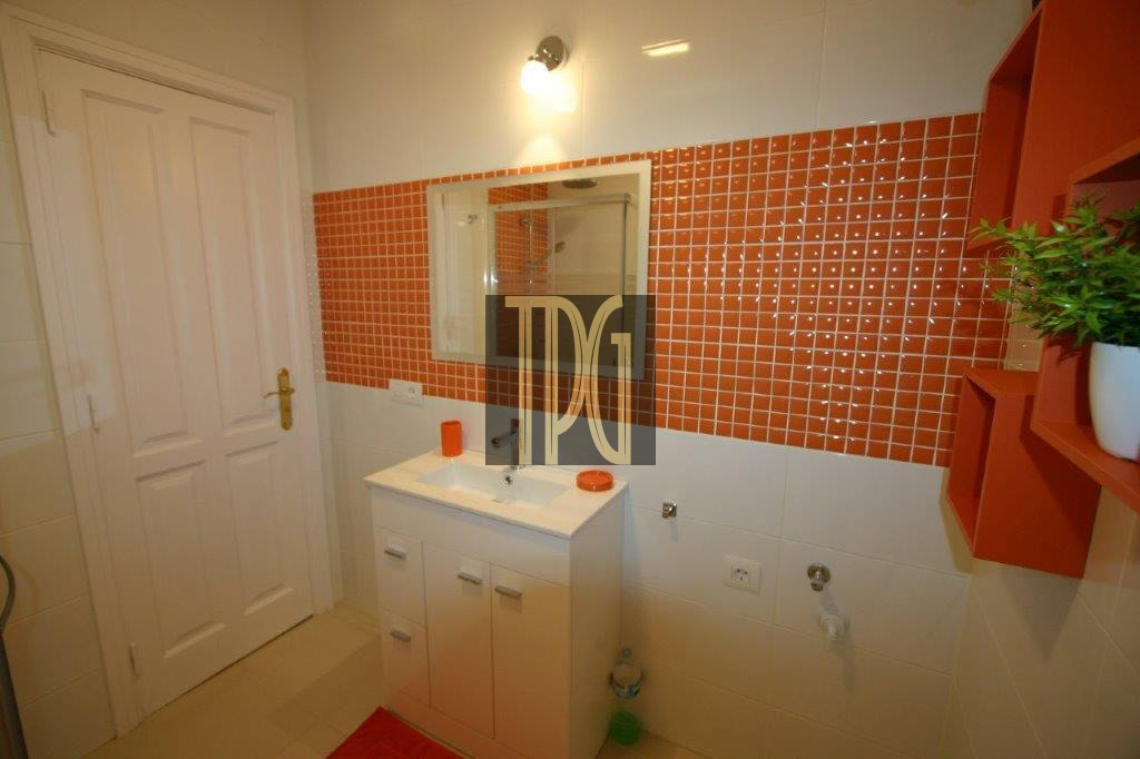 White bathroom vanity with sink in front of an orange mosaic-tile wall and a mirror above it