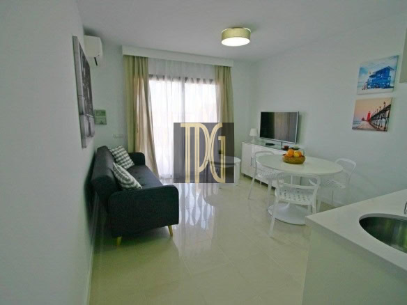 Modern white living room with a black sofa, round dining table, and chairs; window with sheer curtains at the back.