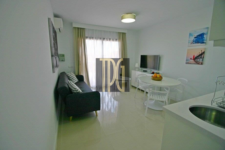 Modern white living room with a black sofa, round dining table, and chairs; window with sheer curtains at the back.