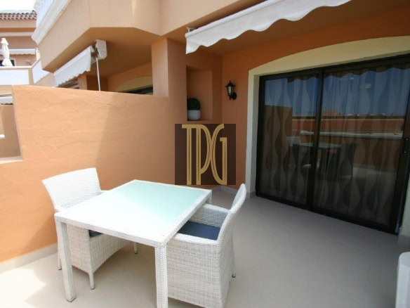 Outdoor balcony seating area with a white wicker table and chairs against orange walls.