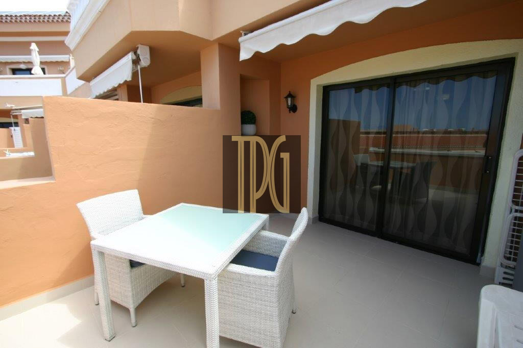 Outdoor balcony seating area with a white wicker table and chairs against orange walls.